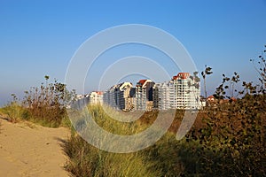 View over sand dunes with grass on coast town against clear blue summer sky - Knokke-Heist, Belgium