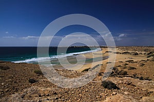 View over sand dunes with green ocean on Playa del Aljibe on white village on steep cliff El Cotillo - North Fuerteventura photo