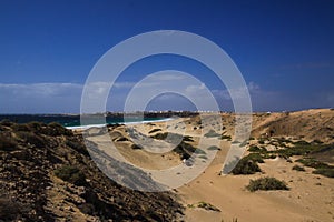 View over sand dunes with green ocean on Playa del Aljibe on white village on steep cliff El Cotillo - North Fuerteventura photo