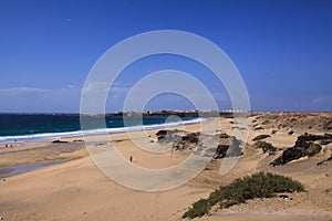 View over sand dunes with green ocean on Playa del Aljibe on white village on steep cliff El Cotillo - North Fuerteventura photo