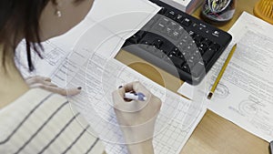 View over the shoulder of a woman doing paper work at the table. Action. Female office worker filling in a form at work.