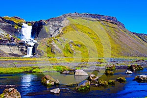 View over small river with boulders and stones on water fall against blue sky