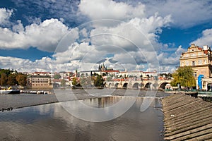 View over Vltava river to Charles bridge, Prague Castle in background under blus sky with white clouds.