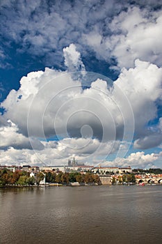 View over Vltava river to Charles bridge, Prague Castle in background under blus sky with white clouds.