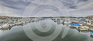 View over a yacht harbor with docked ships in front of clouded sky