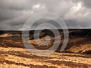 A view of oxenhope moor in west yorkshire with brown dry grass and heather against a grey dramatic cloudy sky