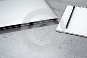 View of a part of a gray desktop with a laptop, notepad and pencil