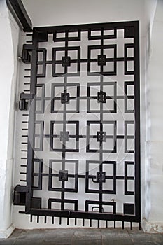 View of a part of an old metal wrought-iron gate in the form of black squares on a white wall background. Architecture