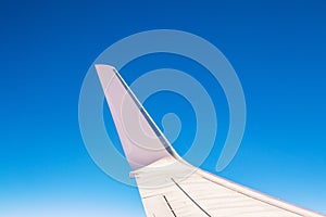 View at the part of a wing of the airplane or airliner during the flight from the window with blue sky and without clouds.Wing of