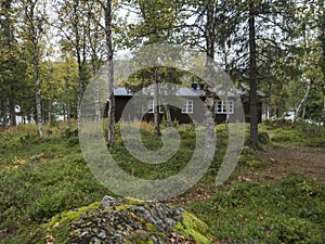 View on Parte Fjallstuga STF mountain cabin hut at Sweden Lapland with Sjabatjakjaure lake, green hills and birch tree. Campsite