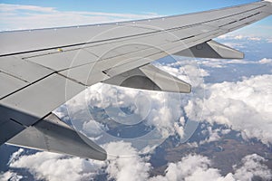 View from passenger window of commercial airplane, clouds on blue sky visible under aircraft wing