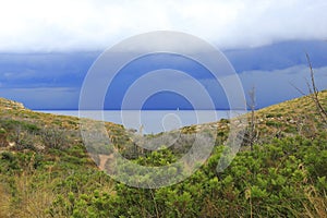 View from the path of the English cemetery. Dramatic sky with rain on Olbia. Cala moresca, Golfo Aranci, Sardinia