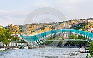 View on the Peace Bridge with the Sololaki Hill and old town buildings on the background, Tbilisi, Georgia