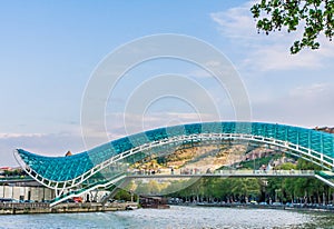 The view on the Peace Bridge with the Sololaki Hill and old town buildings on the background, Tbilisi, Georgia