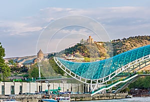 The view on the Peace Bridge with the Sololaki Hill and old town buildings on the background, Tbilisi, Georgia