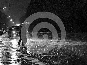 View of a pedestrian crossing in the city at night during a heavy downpour. Silhouettes of people with umbrellas.