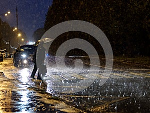 View of a pedestrian crossing in the city at night during a heavy downpour. Silhouettes of people with umbrellas. photo