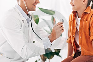 View of pediatrist in white coat examining kid with stethoscope