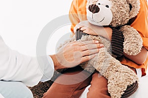 View of pediatrist in white coat and kid with teddy bear isolated on white
