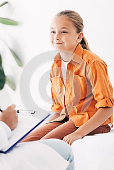 View of pediatrist writing in clipboard while examining child in clinic