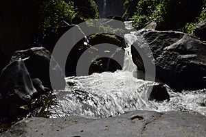 View of Peguche Waterfall in the mountains. It's surrounded by green forest full of vegetation. Ecuador