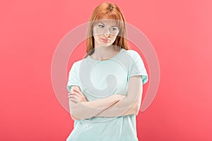 View of pensive redhead young woman in t-shirt standing with crossed arms and looking away isolated on pink