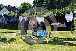 View of people hanging laundry on clothesline in backyard with houses and trees in background