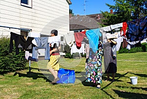 View of people hanging laundry on clothesline in backyard with houses and trees and clear blue sky background