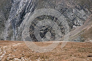 View of People walking in front a big wall of a high mountain in a landscape in the Pyrenees photo