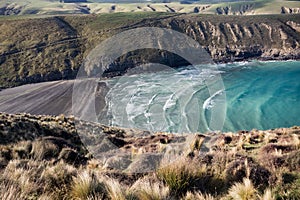 View on periodic waves in rocky Tumbledown bay with black sand beach on Banks Peninsula