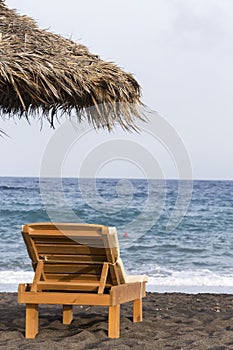 view of Perissa beach on the Greek island of Santorini with sunbeds and umbrellas. Beach is covered with fine black sand, and