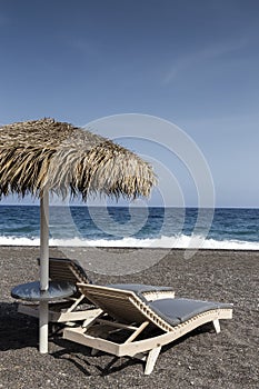 view of Perissa beach on the Greek island of Santorini with sunbeds and umbrellas. Beach is covered with fine black sand, and