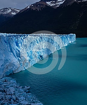 A view of the Perrito Moreno glacier, in Argentina, with clouds reflections on the lake and a mountain in the background