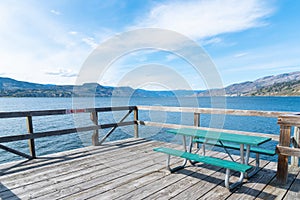 Picnic table on Naramata Wharf with scenic view of Okanagan Lake, mountains, and blue sky