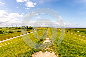 view on Pilsum lighthouse in the landscape of East Frisia with tourists walking around the dike and taking photographs