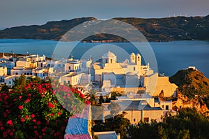 View of Plaka village on Milos island over red geranium flowers on sunset in Greece