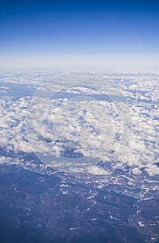 View from a plane window on clouds and blue clear sky and the earth from height. Beautiful view from air of mountains.