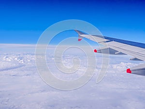 View from a plane window: a plane wing over clouds and blue sky