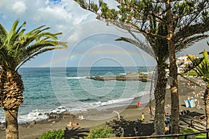 View of the Playa de la Arena and rainbow over the sea, the phenomenon of nature, bright colors on the rainbow and cloudy sky