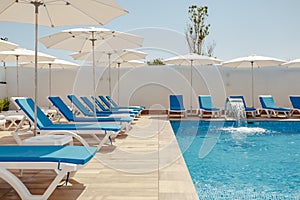 view of the pool with blue water, sun loungers and umbrellas