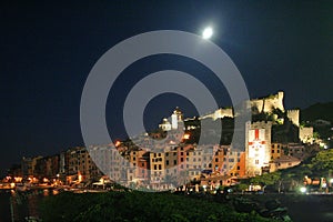 View of Portovenere`s buildings at night under the moon with a castle, tower and cathedral illuminated