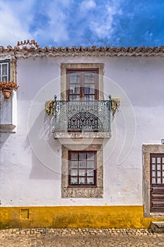 View of a Portuguese vernacular facade with balcony and flowers around windows, on medieval village of Ãƒâ€œbidos