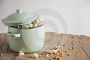 View of pot with freshly popped popcorn on rustic wooden table, white background, horizontal