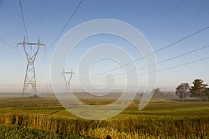 View of power line towers in farmland fields during a beautiful misty late summer golden hour morning