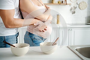 View of pregnant couple hugging in kitchen with cereals in bowls