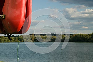View of a quiet lake with red throw buoy on the foreground