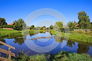 View on quiet peaceful place at dutch hiking trail with idyllic river, lush green meadow and trees against deep blue cloudless