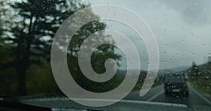 View through a rainy windshield on a gloomy day. Driving in rain and travel safety concept. Blurred road scene for