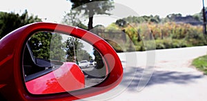 View of rear car in side mirror of red cabriolet at speed