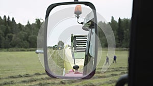 View on rear mirror from agriculture tractor cabin driving at farm grass margine